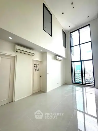 Spacious modern living room with high ceilings and large windows offering city views.