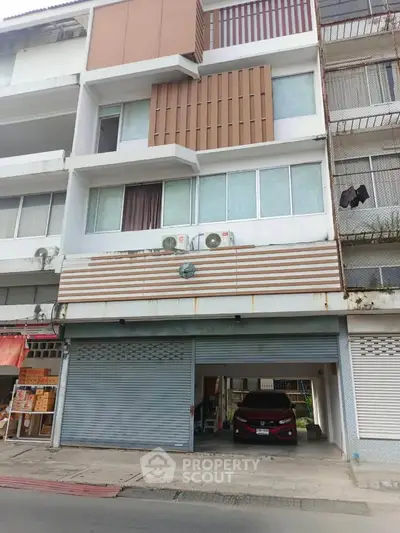 Modern multi-story building with parking space and air conditioning units, ideal for urban living.