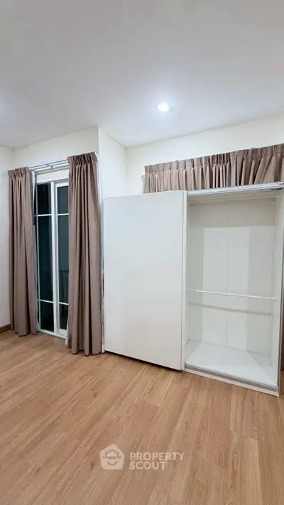 Spacious bedroom with wooden flooring and large window, featuring a modern white wardrobe.