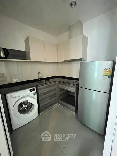 Modern kitchen with sleek cabinets, washing machine, and stainless steel fridge in a compact layout.