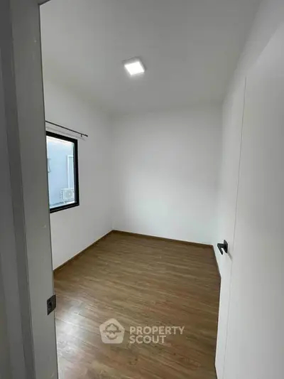 Spacious empty room with wooden flooring and a large window, perfect for customization.