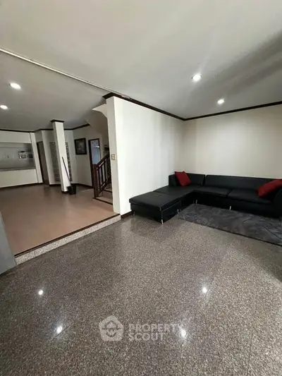 Spacious living room with modern black sectional sofa and polished flooring, ideal for family gatherings.