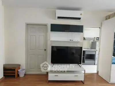 Modern living room with sleek TV stand and air conditioning, adjacent to a compact kitchen.