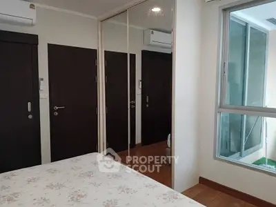 Cozy bedroom with mirrored closet and large window in modern apartment.