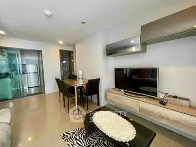 Modern living room with sleek furniture and open layout, featuring a TV and dining area.