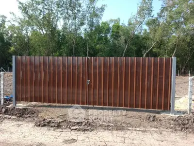 Sturdy metal gate with secure lock in a rural setting, surrounded by lush greenery and open land.