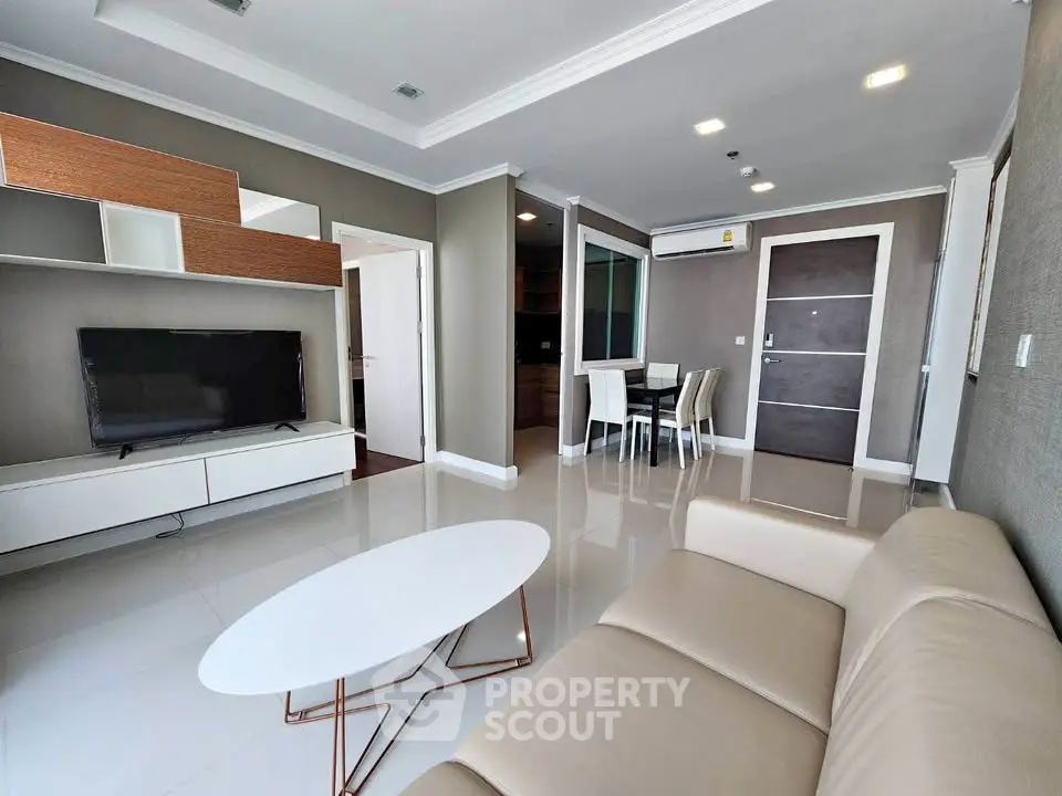 Modern living room with sleek furniture and open layout, featuring a TV and dining area.