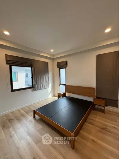 Spacious bedroom with wooden flooring and modern bed frame, ample natural light from large windows.