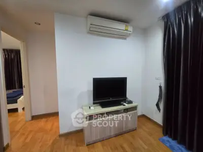 Modern living room with air conditioning and TV unit, featuring wooden flooring and elegant curtains.