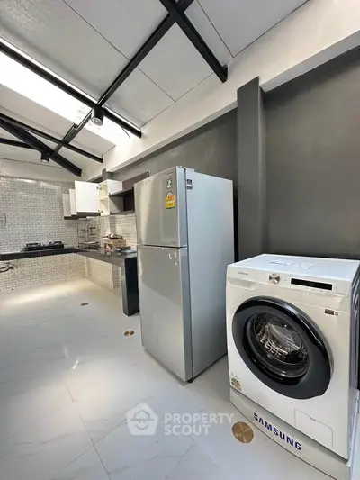 Modern kitchen with sleek appliances and open layout, featuring a fridge and washing machine under natural light.