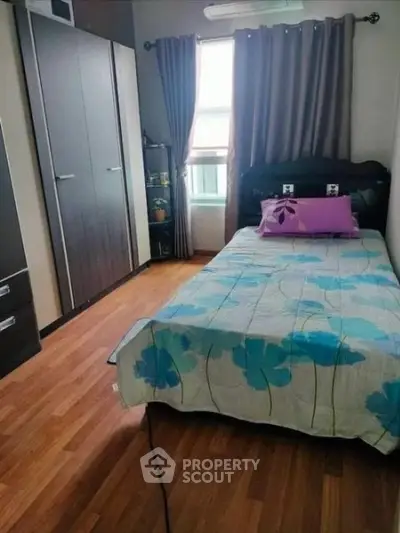 Cozy bedroom with wooden flooring, stylish wardrobe, and a single bed with floral bedding.