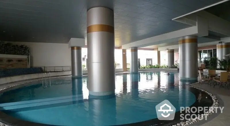 Luxurious indoor pool with elegant pillars and ample lounging space, perfect for relaxation and entertainment in a high-end residential complex.