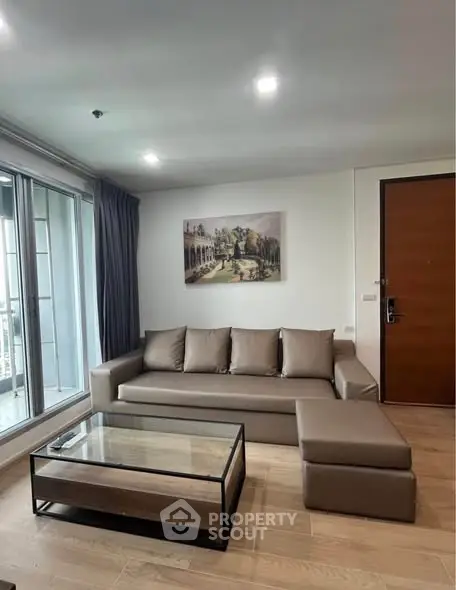 Modern living room with sleek sofa and glass coffee table, featuring a large window and stylish decor.