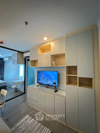 Modern living room with built-in storage and TV, adjacent to a cozy bedroom with glass partition.