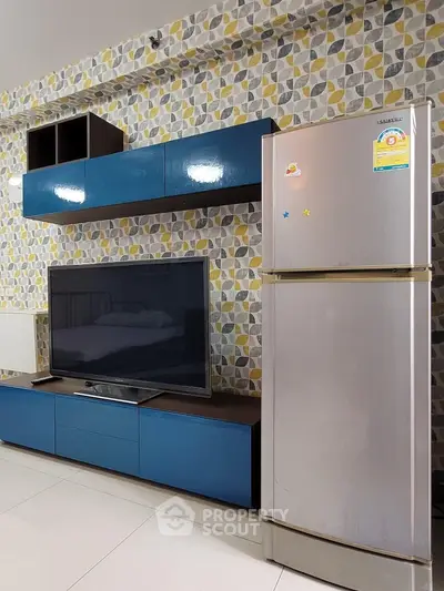 Modern living room with stylish TV unit and refrigerator, featuring geometric wallpaper.