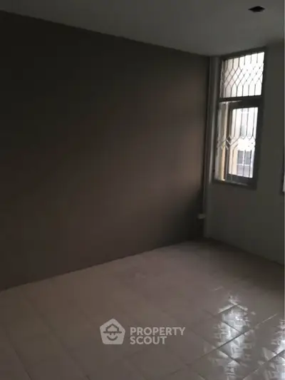 Spacious unfurnished room with tiled floor and large window, ideal for customization.