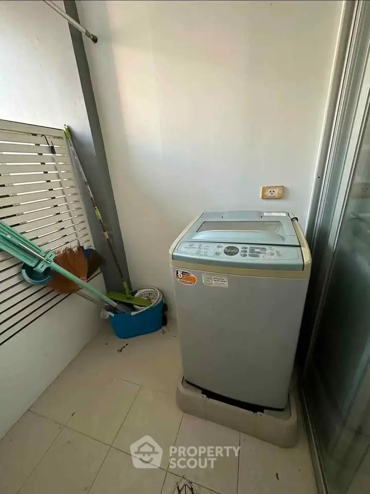 Compact laundry area with washing machine and cleaning tools in a modern apartment.