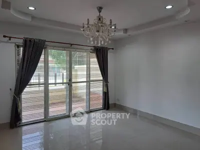Spacious living room with elegant chandelier and large windows opening to a patio.