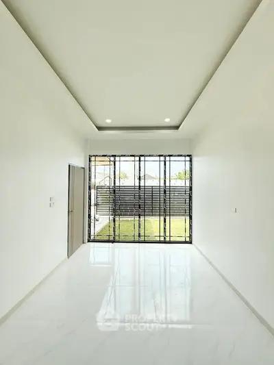 Spacious modern living room with large windows and garden view, featuring sleek white walls and ceiling lights.