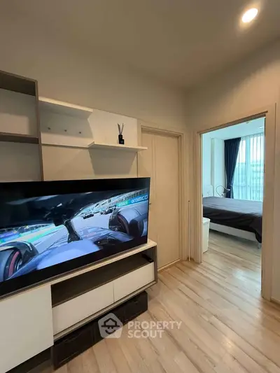 Modern apartment interior with TV and bedroom view, featuring sleek wooden flooring and stylish decor.
