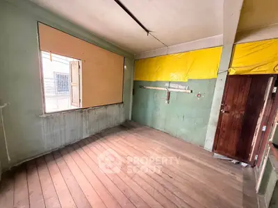 Spacious room with wooden flooring and large window, ideal for renovation.