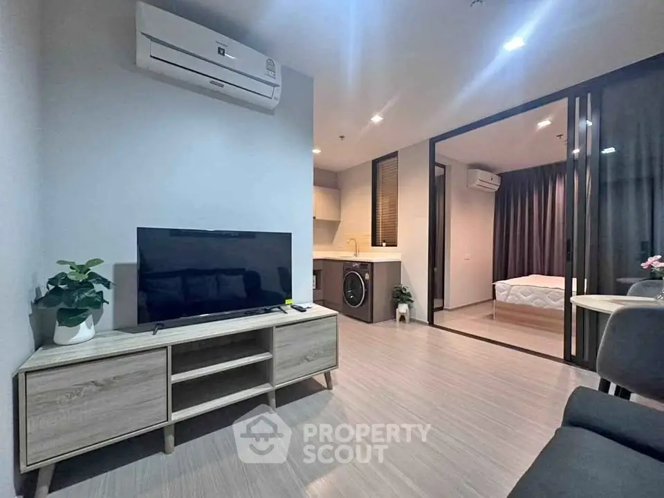 Modern living room with TV, air conditioning, and view into bedroom and kitchen.