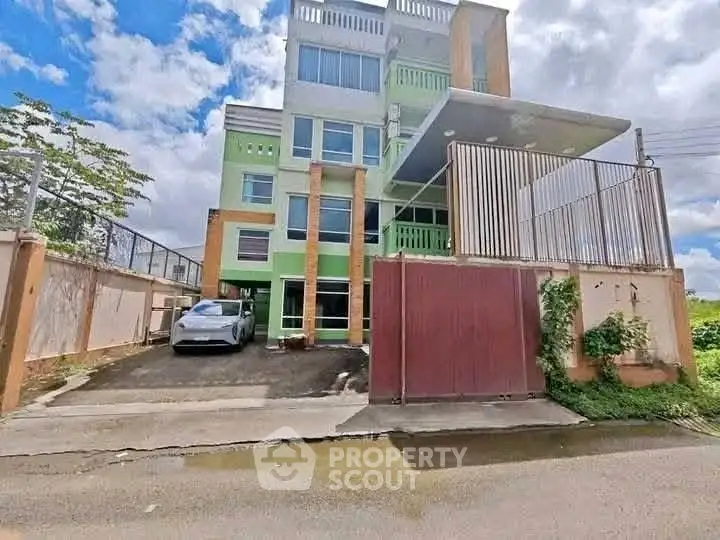 Modern multi-story building with gated parking and vibrant facade under a clear sky.