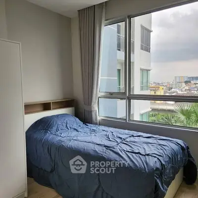 Cozy bedroom with large window offering city views, perfect for urban living.