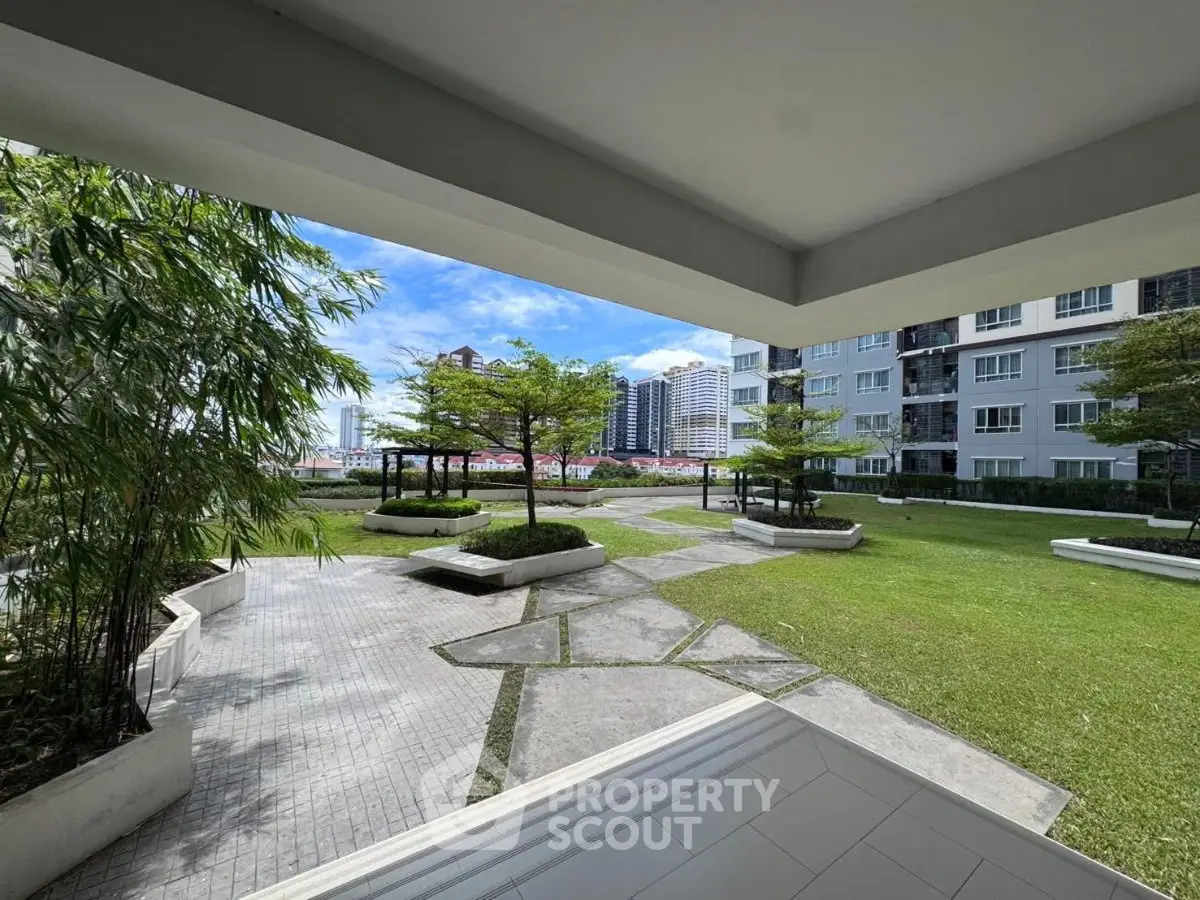 Spacious garden view from modern apartment building with lush greenery and city skyline.