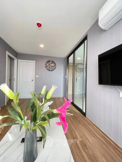 Modern living room with stylish decor and wooden flooring, featuring a wall-mounted TV and air conditioning.