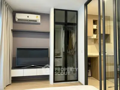 Modern bedroom with TV and wardrobe, adjacent to a compact kitchen area.