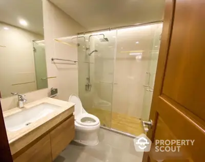 Modern bathroom with glass shower enclosure and wooden vanity in luxury apartment.