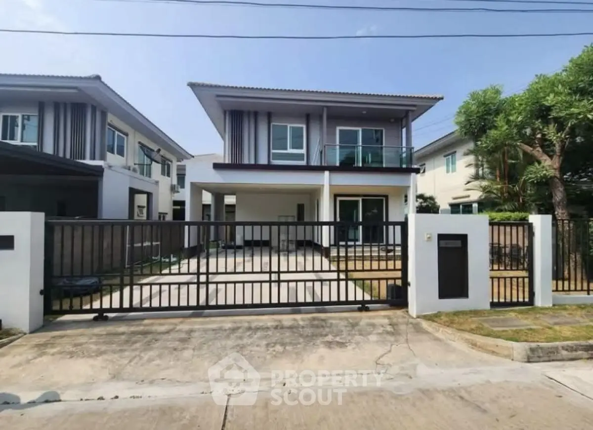 Modern two-story house with gated driveway and balcony in suburban neighborhood.