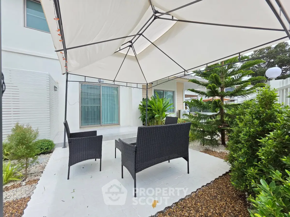 Charming outdoor patio with canopy and wicker furniture in lush garden setting.