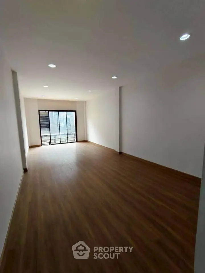 Spacious empty room with wooden flooring and large window, ideal for customization.