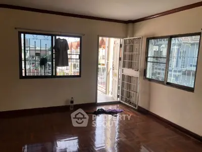 Spacious empty room with polished wooden floors and balcony access, offering potential for customization.