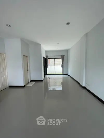 Spacious empty living room with glossy floors and large window for natural light.