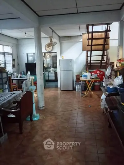Spacious open-layout living area with tiled flooring and a staircase, featuring a fridge and ample natural light.