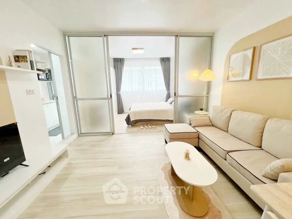 Modern open-plan living room with cozy sofa and stylish decor leading to a bright bedroom.