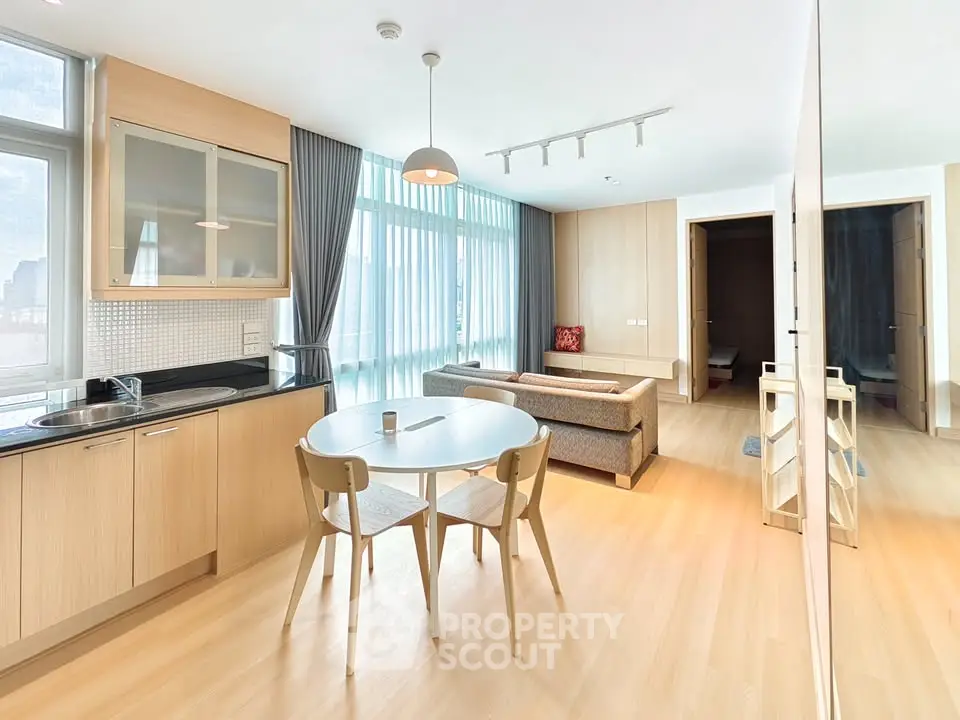 Modern open-plan living room with kitchen, featuring sleek furniture and large windows.