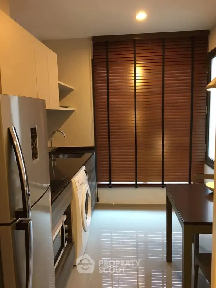Modern kitchen with sleek appliances and stylish blinds, featuring a washing machine and fridge.