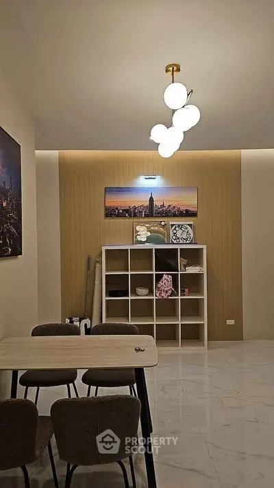 Modern dining area with stylish lighting and wall art, featuring a sleek table and chairs on marble flooring.