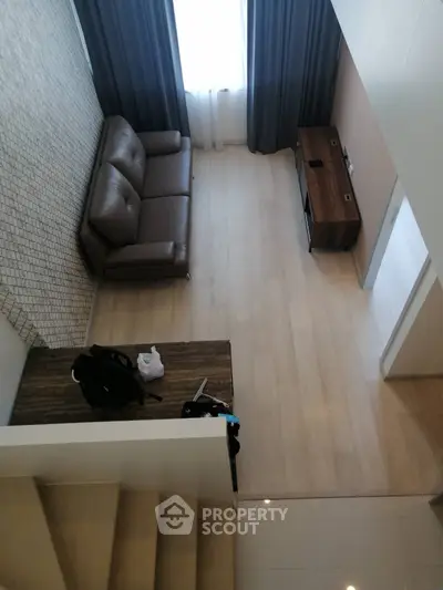 Modern living room with stylish brown sofa and wooden TV stand, featuring elegant flooring and large window.