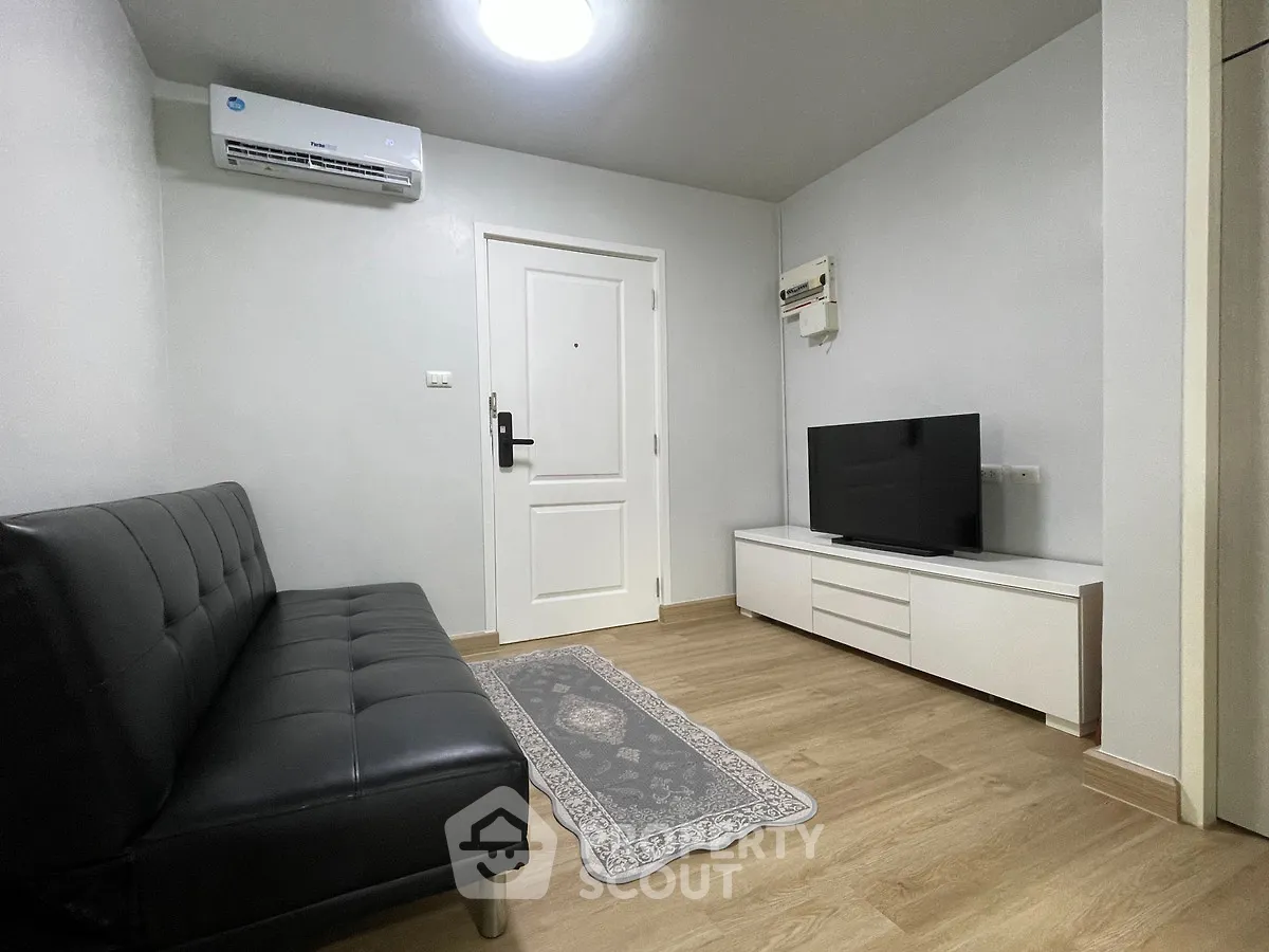 Modern living room with sleek black sofa and flat-screen TV on wooden flooring.
