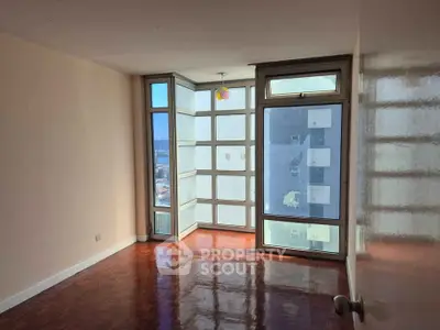 Spacious empty room with large windows and polished wooden floors in a modern apartment.