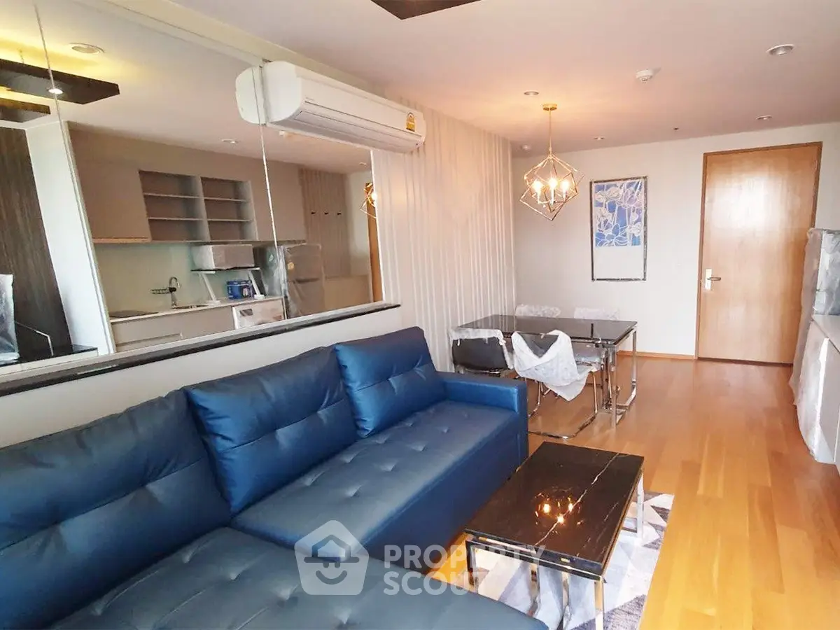 Modern living room with blue sofa, dining area, and stylish lighting in open-plan apartment.