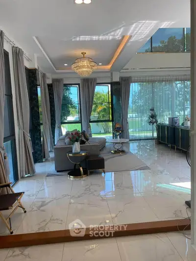 Luxurious living room with high ceilings, elegant chandelier, and large windows offering stunning garden views.