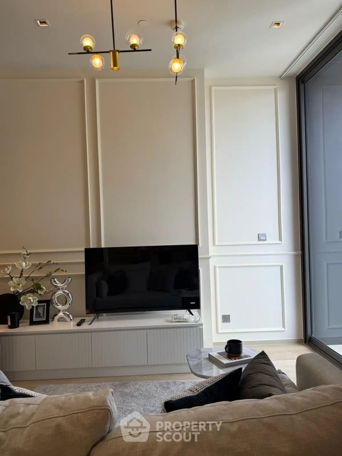 Modern living room with stylish decor and large TV, featuring elegant lighting and cozy seating.