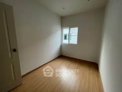 Spacious empty room with wooden flooring and natural light from window