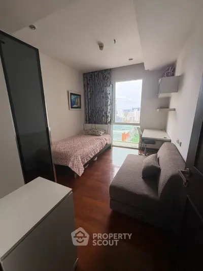 Cozy bedroom with city view, featuring a bed, sofa, and desk, perfect for urban living.